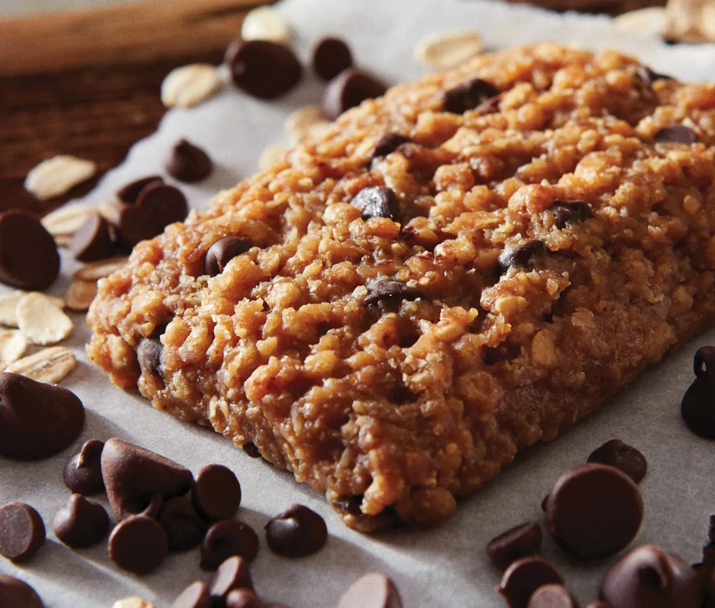 An unwrapped Clif Bar Chocolate Chip on baking paper, surrounded by chocolate chips and rolled oats